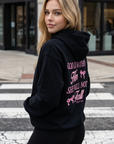 Woman wearing a black hoodie with pink text on a city street