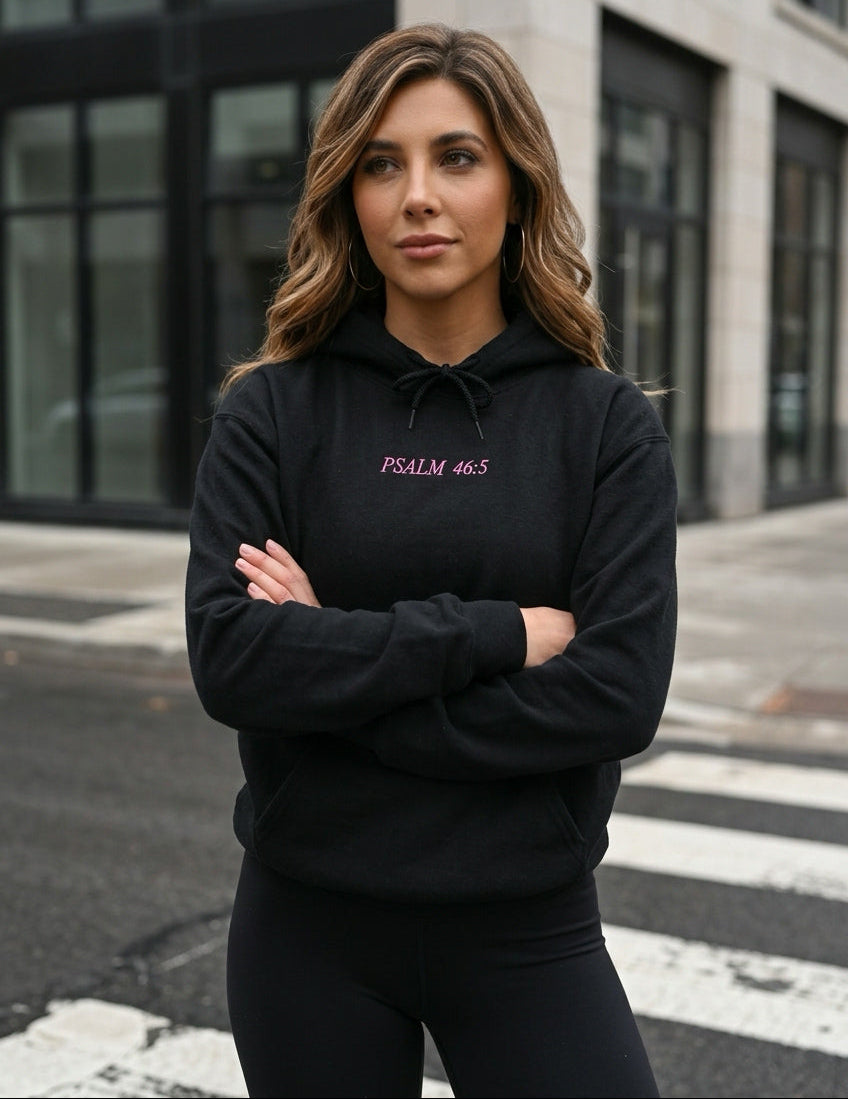 Woman wearing a black hoodie with text, standing on a street with a building in the background