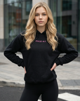 Woman wearing a black hoodie with text, standing on a street.