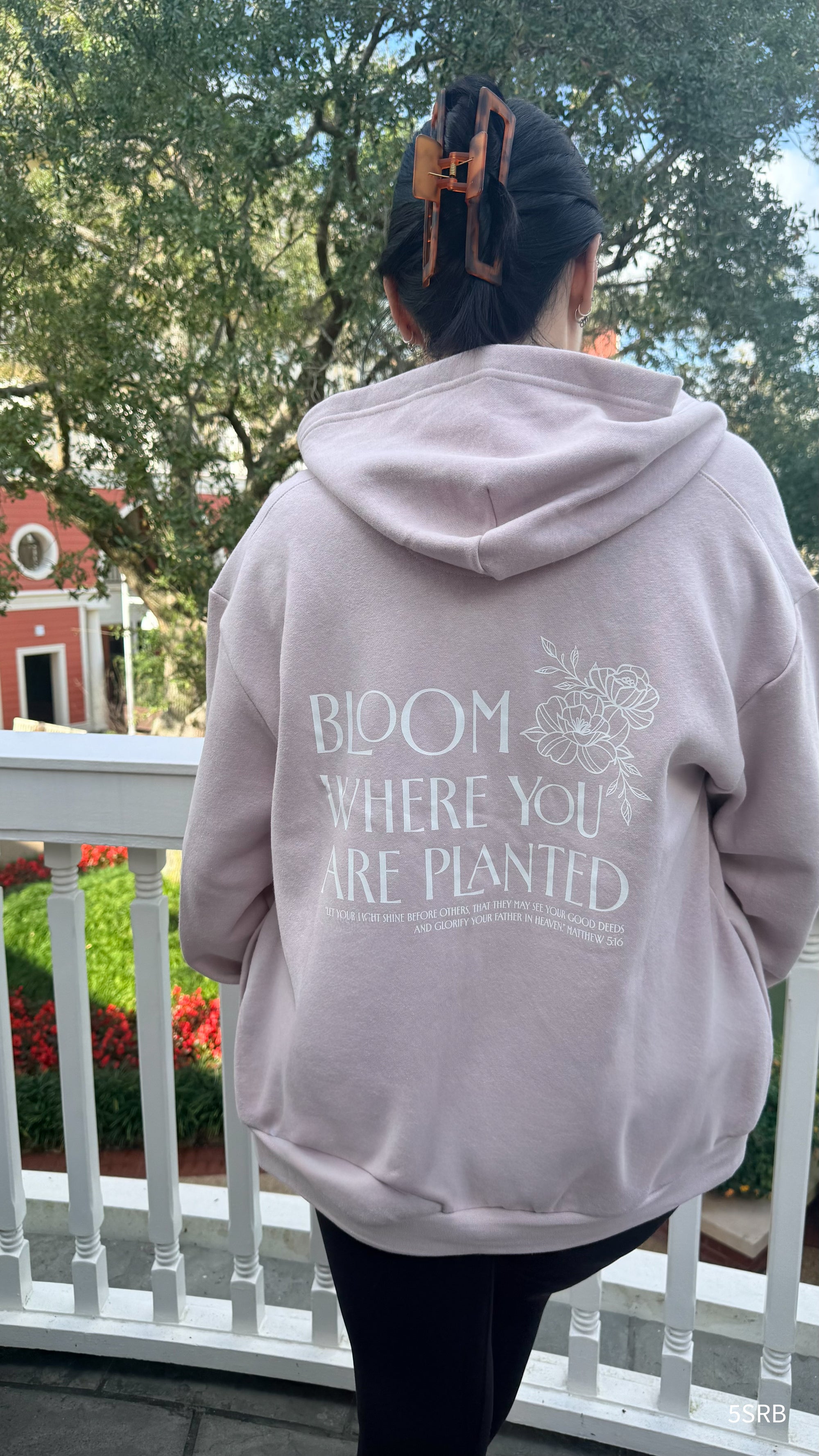Person wearing a light pink hoodie with text on the back, standing outdoors.
