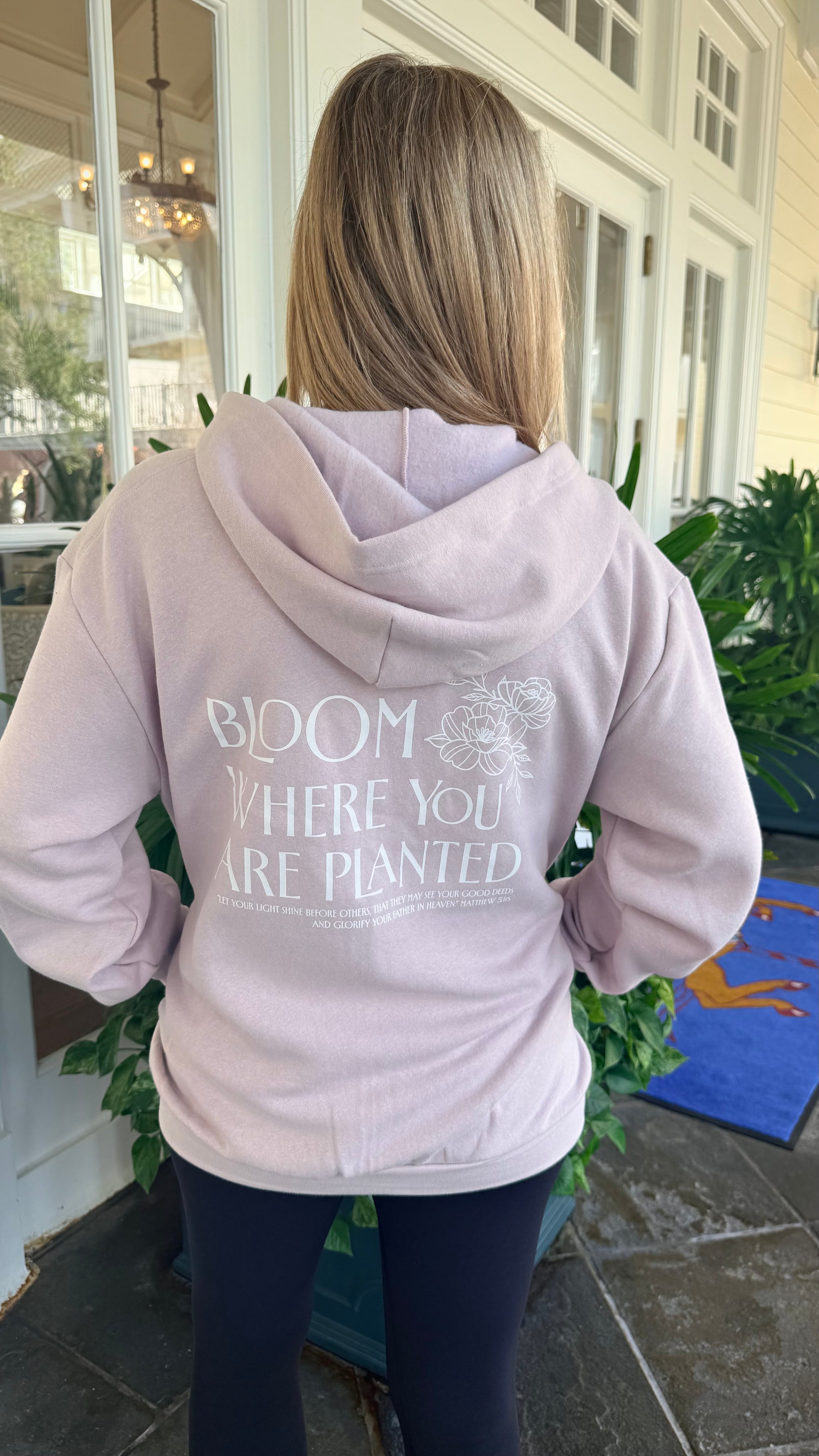 Person wearing a light pink hoodie with text on the back, standing outdoors.