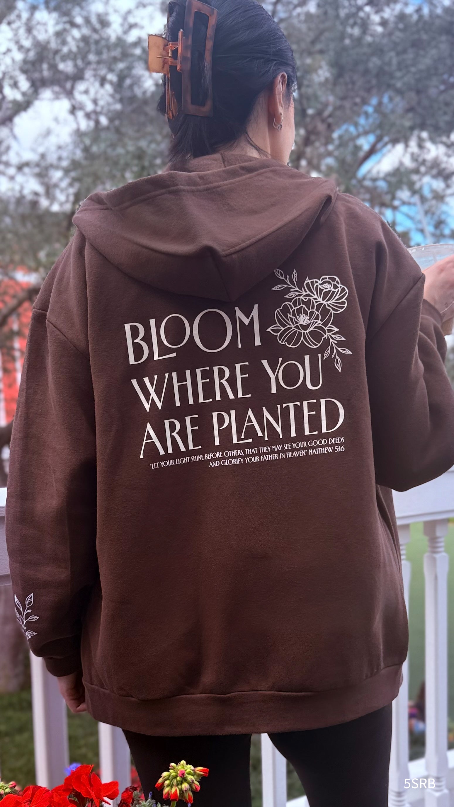 Person wearing a brown hoodie with 'Bloom Where You Are Planted' text on the back.