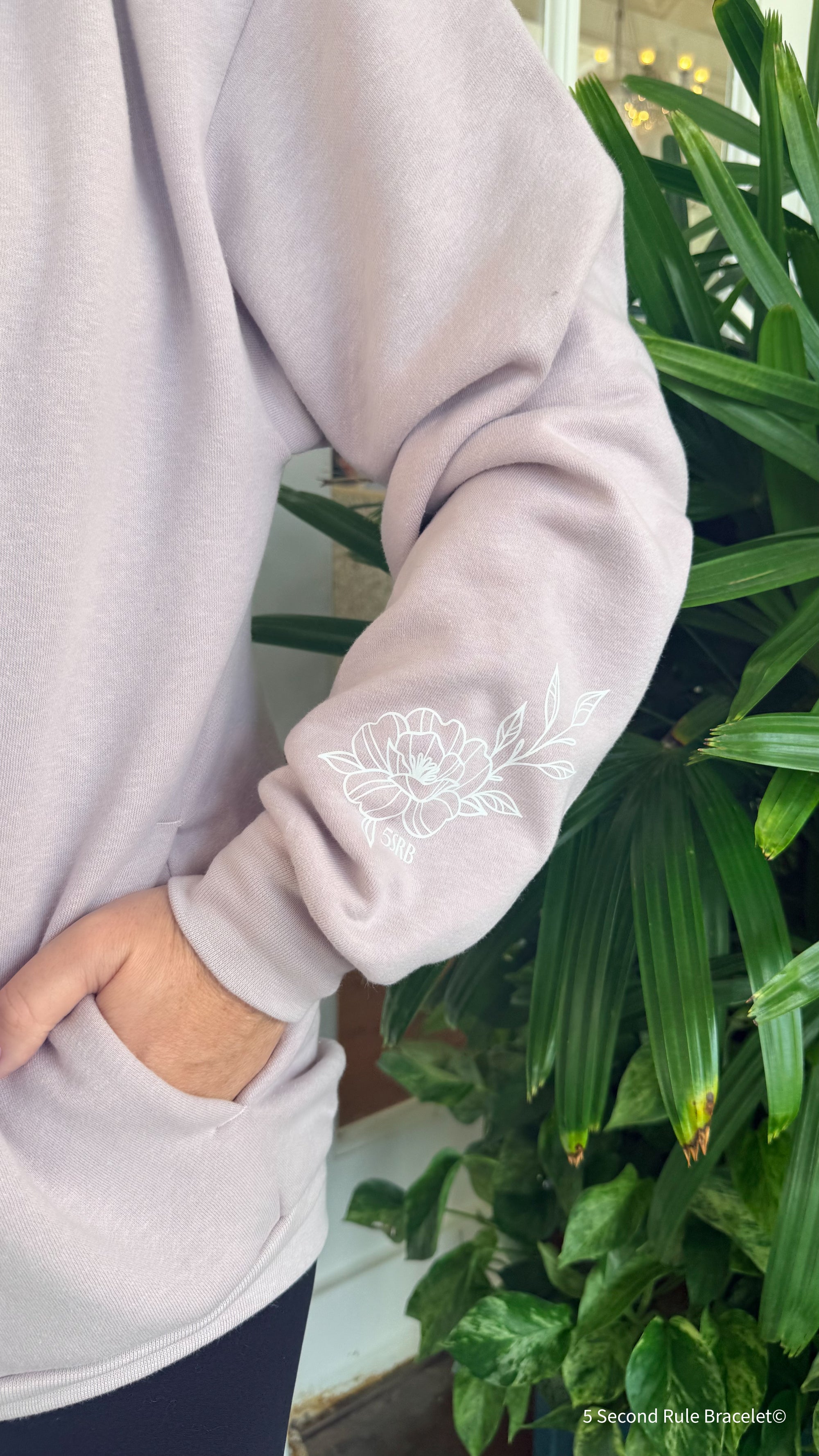 Light gray sweatshirt with white floral embroidery against a green plant background