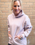 Woman wearing a light pink hoodie standing against a brick wall.