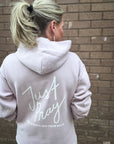 Person wearing a light gray hoodie with 'Just Pray' text on the back, standing against a brick wall.