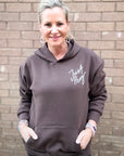 Woman wearing a brown hoodie with 'Just Pray' text against a brick wall.