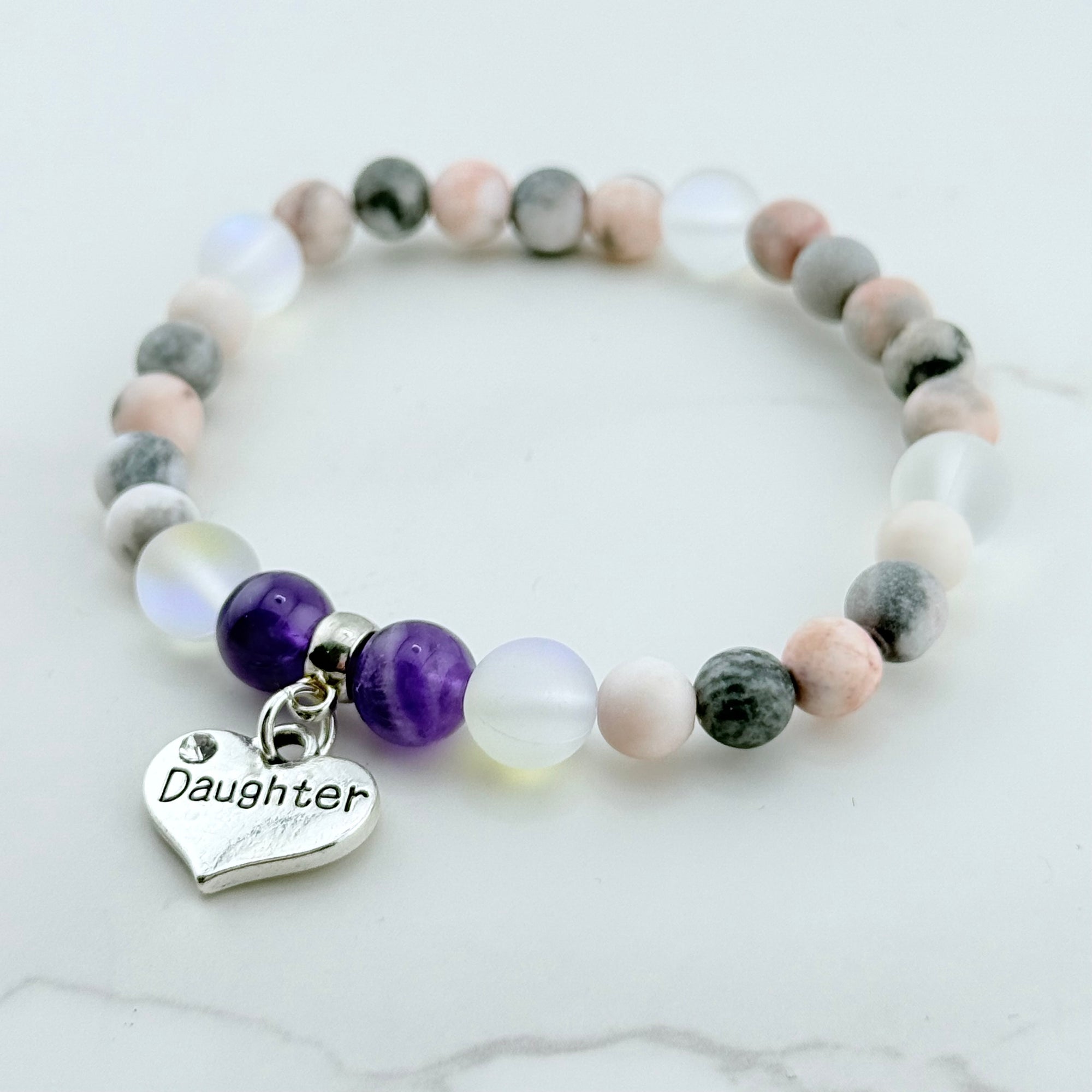 Beaded bracelet with a 'Daughter' charm on a marble surface
