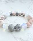 A bracelet with silver-colored druzies and pink zebra jasper beads on a marble surface.