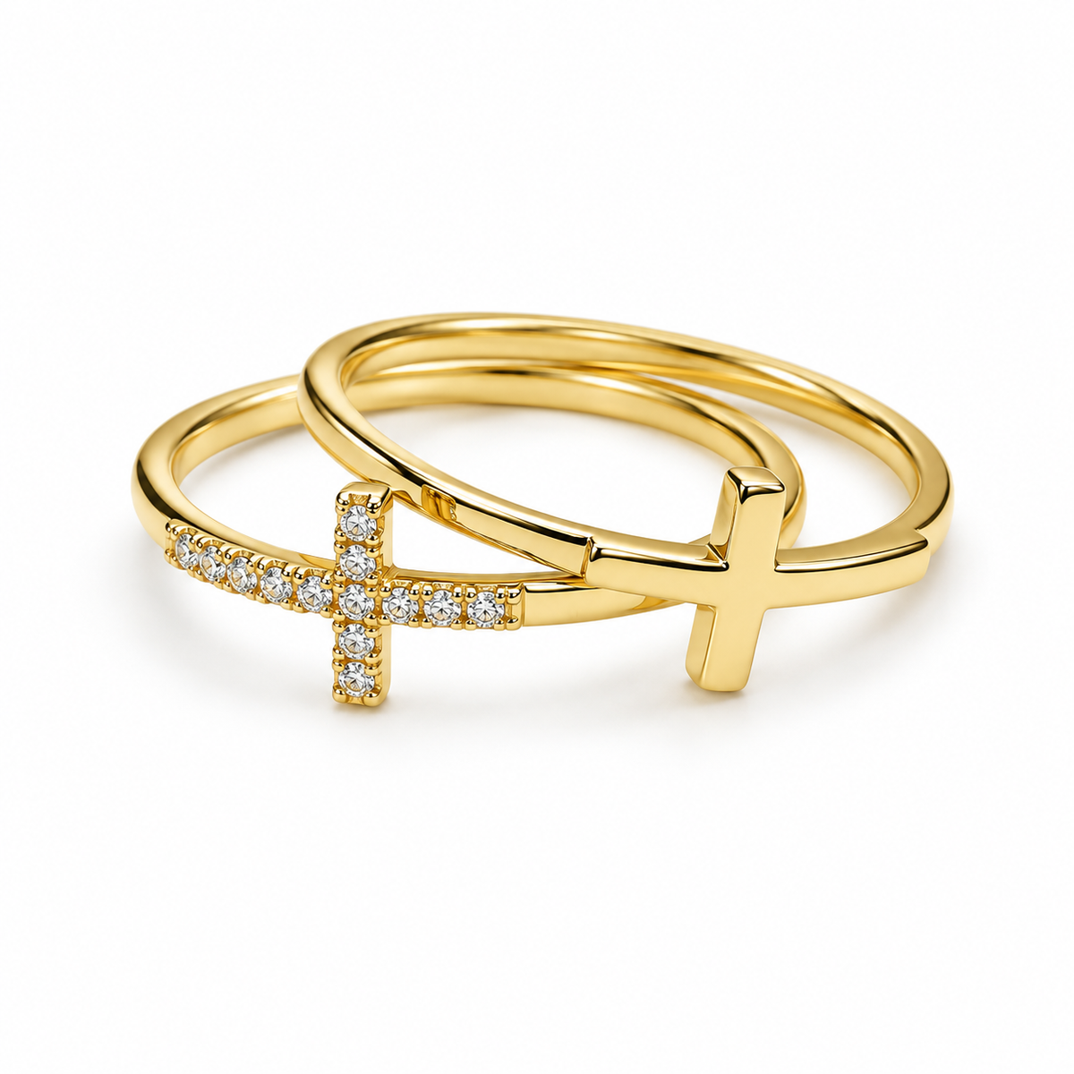 A pair of gold rings, one featuring a cross pavé-set with small clear stones and the other a solid cross pendant, displayed on a clean white background.