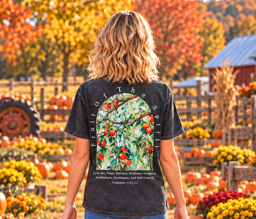 A woman viewed from behind walking through a pumpkin patch, wearing a dark gray mineral-washed graphic t-shirt with a large back print of a apple tree with a bible verse