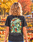A woman viewed from behind walking through a pumpkin patch, wearing a dark gray mineral-washed graphic t-shirt with a large back print of a apple tree with a bible verse