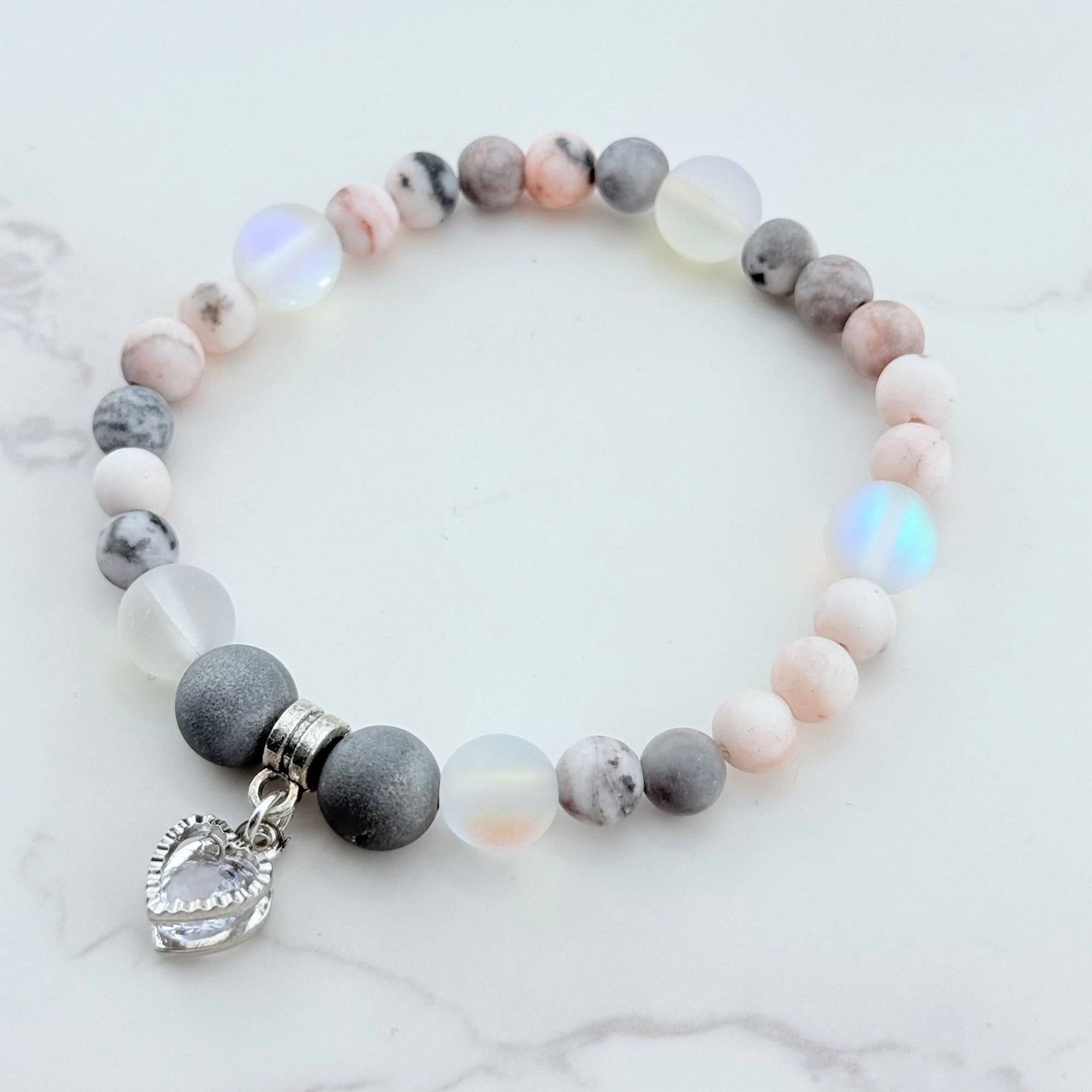 Beaded bracelet with gray, pink, and white beads and a heart charm on a marble surface.