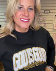 Woman wearing a black sweatshirt with 'God is Good all the time' text in gold.