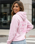 Woman wearing a pink hoodie with text on the back, standing outdoors.