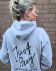 Person wearing a gray hoodie with 'Just Pray' text on the back against a brick wall.