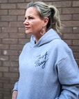 Woman wearing a gray hoodie with 'Just Stay' text against a brick wall.