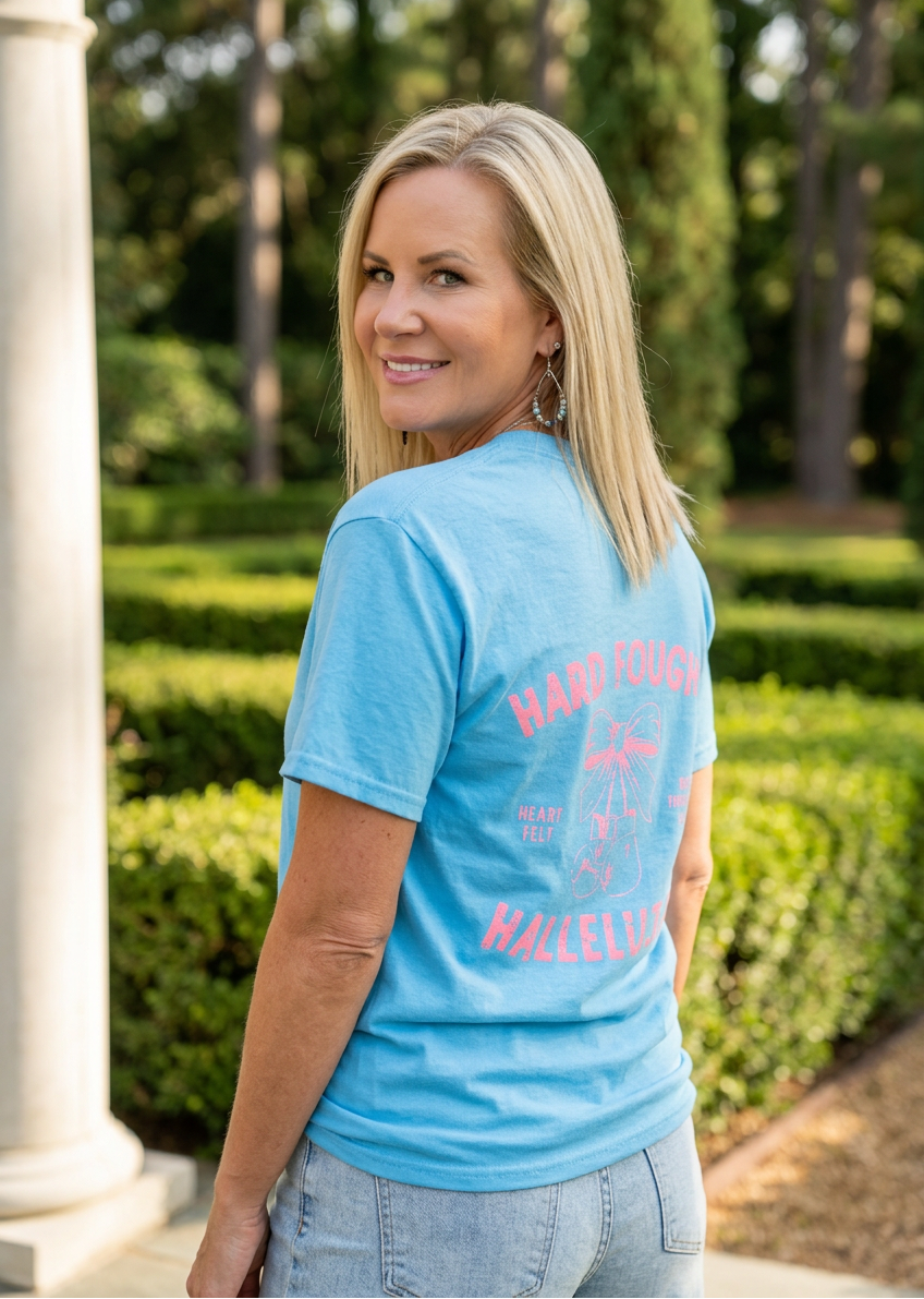 Woman wearing a blue t-shirt with text, standing outdoors with greenery in the background
