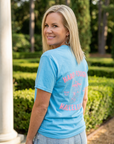 Woman wearing a blue t-shirt with text, standing outdoors with greenery in the background