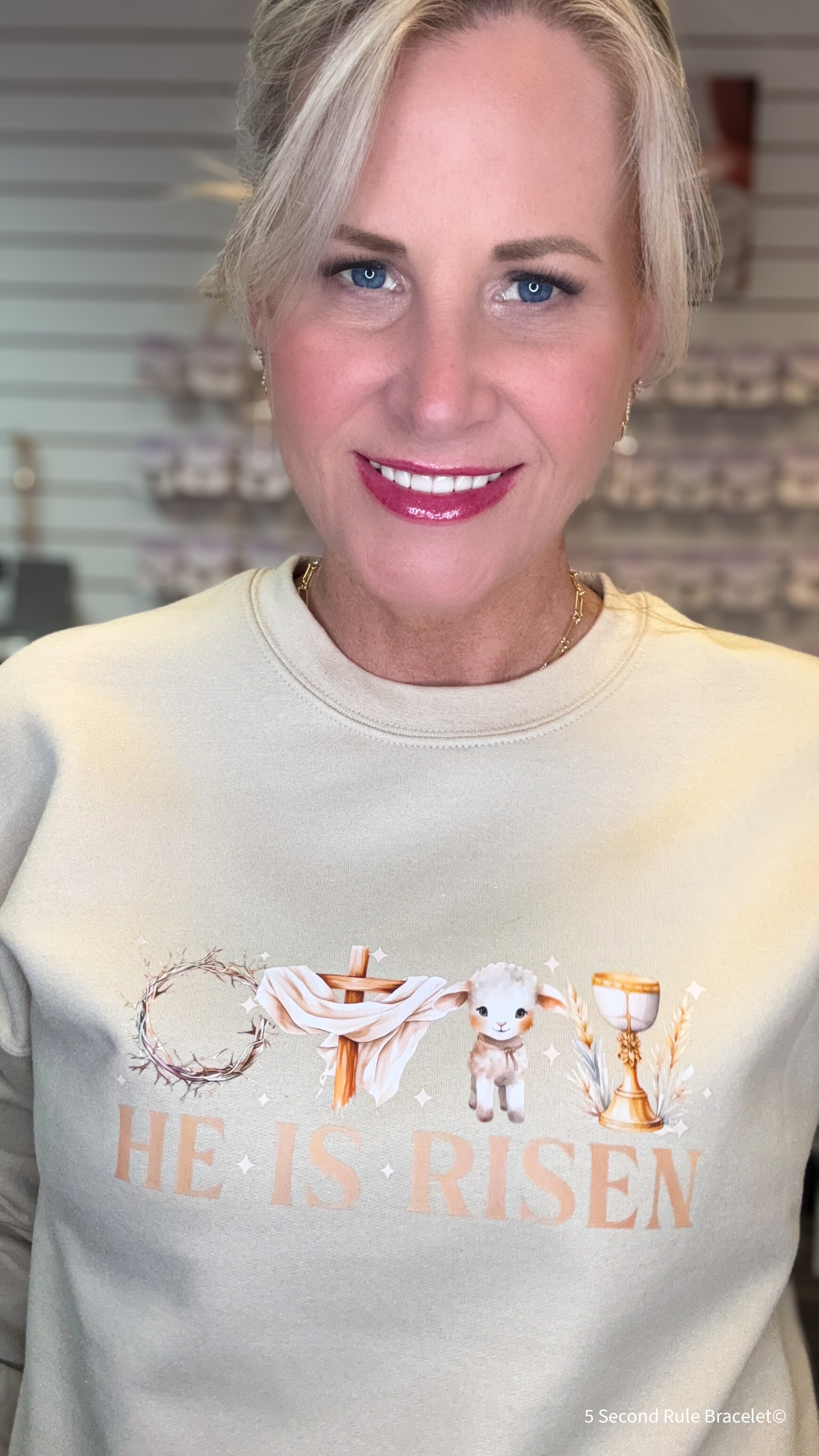 Woman wearing a light-colored sweatshirt with 'He is Risen' text and lamb graphic.