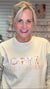 Woman wearing a light-colored sweatshirt with 'He is Risen' text and images.