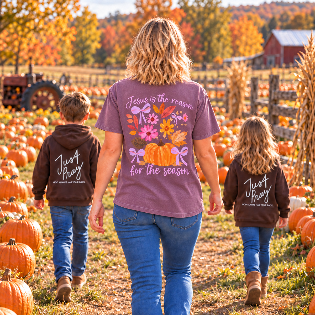A woman and two children walk away in a pumpkin patch wearing matching brown hoodies with white 'Just Pray' text on the back. The woman's tee features a large colorful autumn graphic with pumpkins, flowers, and the phrase 'Jesus is the reason for the season.