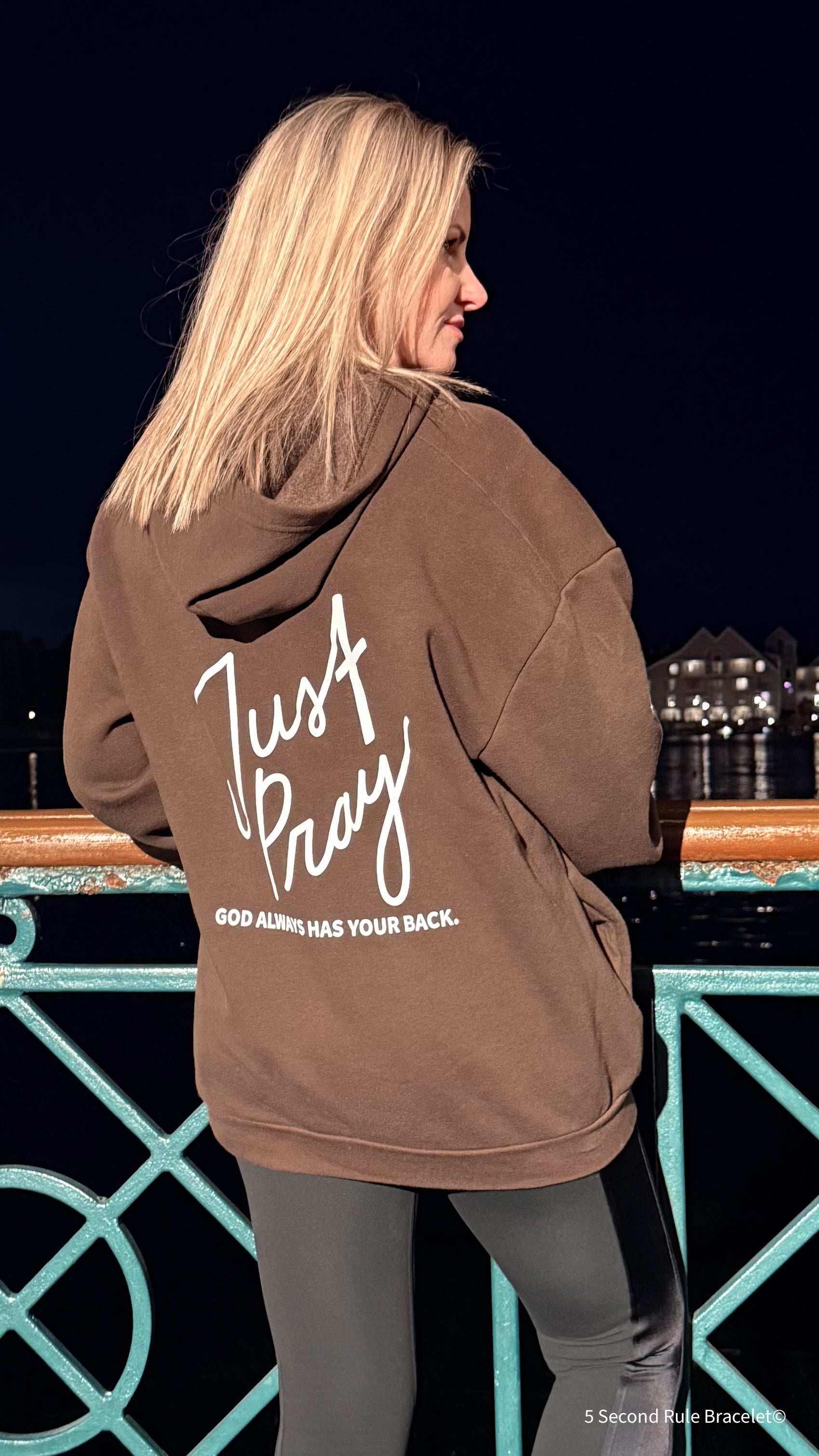 Person wearing a brown hoodie with text on the back, standing by a poolside at night.