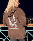 Person wearing a brown hoodie with text on the back, standing by a poolside at night.
