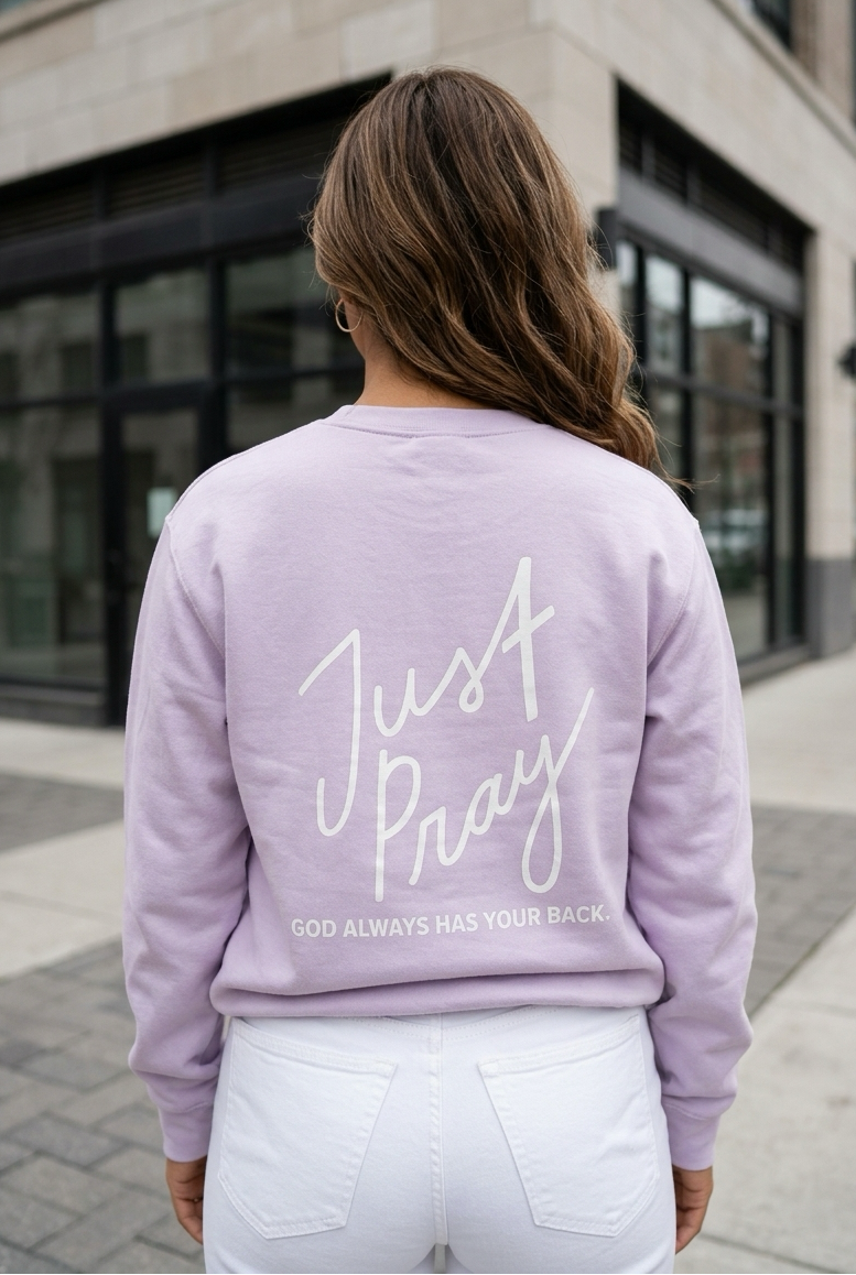 Person wearing a lavender sweatshirt with 'Just Pray' text, standing on a sidewalk.
