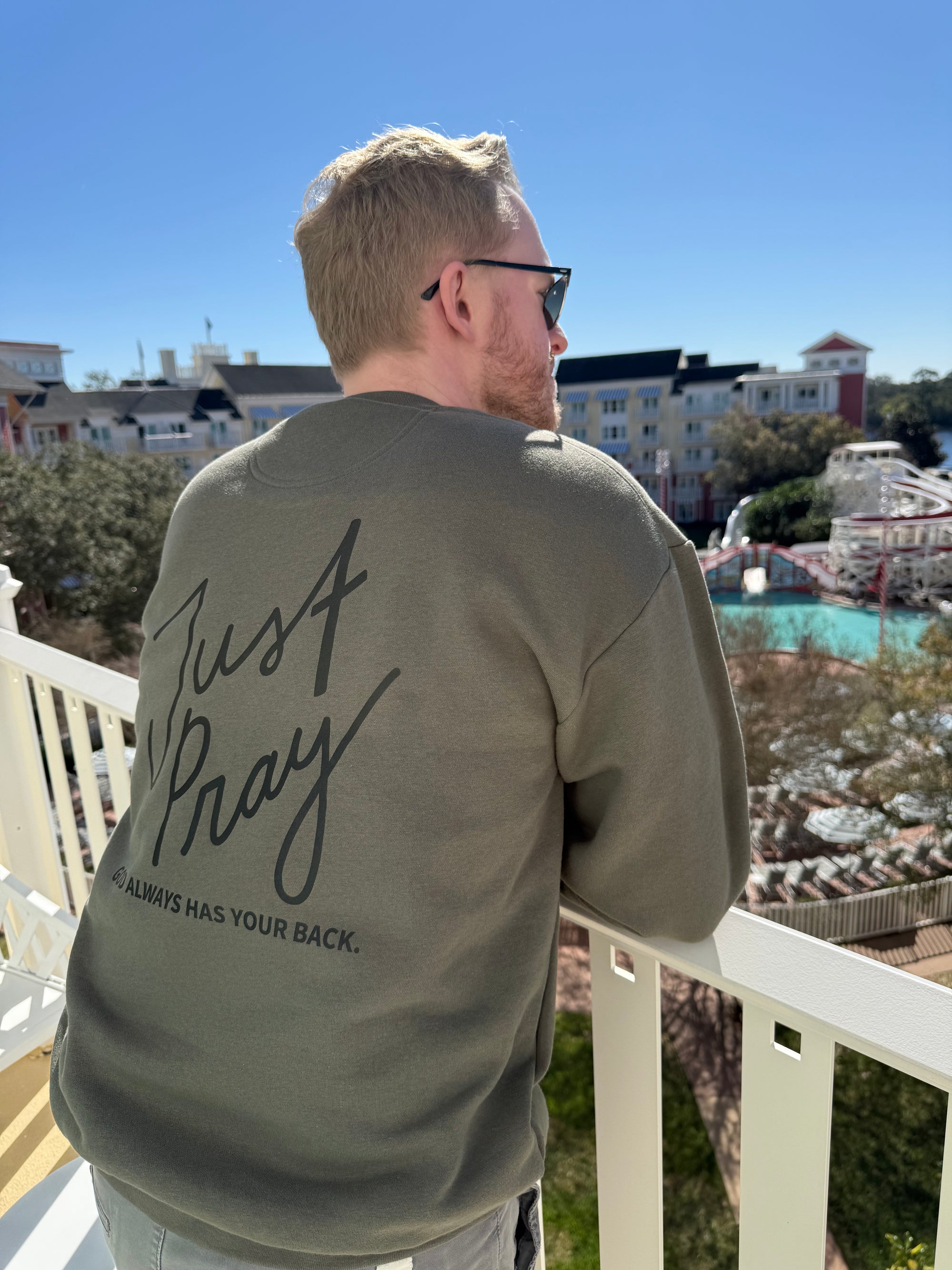Man wearing a sweatshirt with 'Just Pray' text on a balcony overlooking a scenic area.