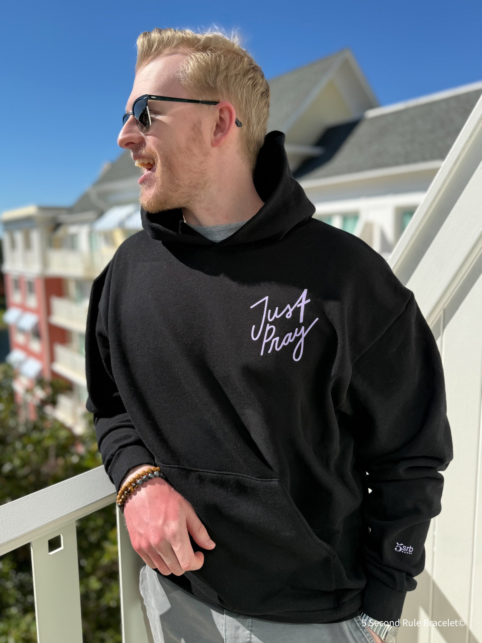 Man wearing a black hoodie with 'Just Stay' text on a balcony
