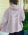 Person wearing a light pink hoodie with 'Just Pray' text on the back, standing outside.