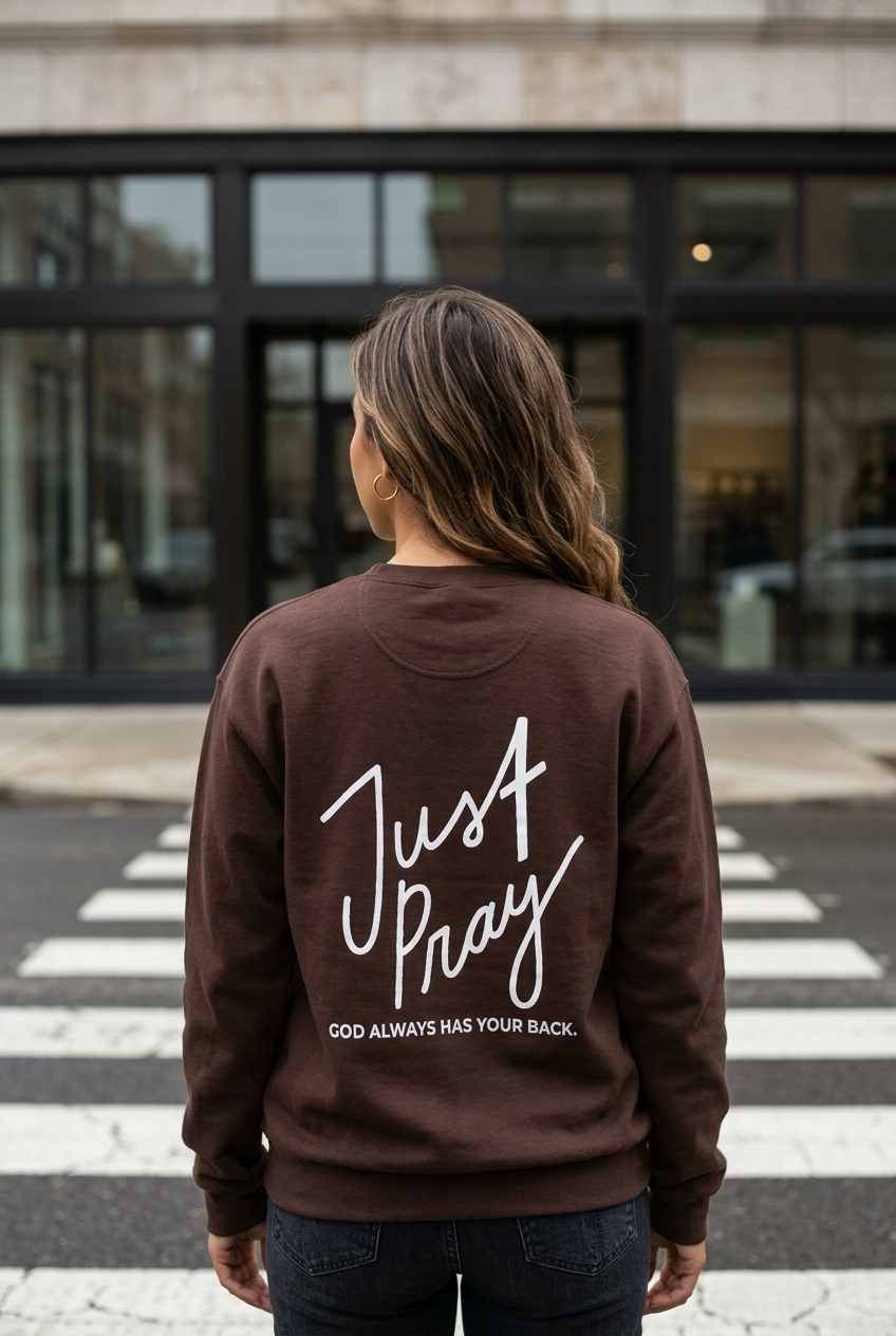 Person wearing a brown sweatshirt with 'Just Pray' text on the back, standing on a crosswalk.