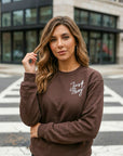 Woman wearing a brown sweatshirt with 'Just Pray' text, standing on a city street.