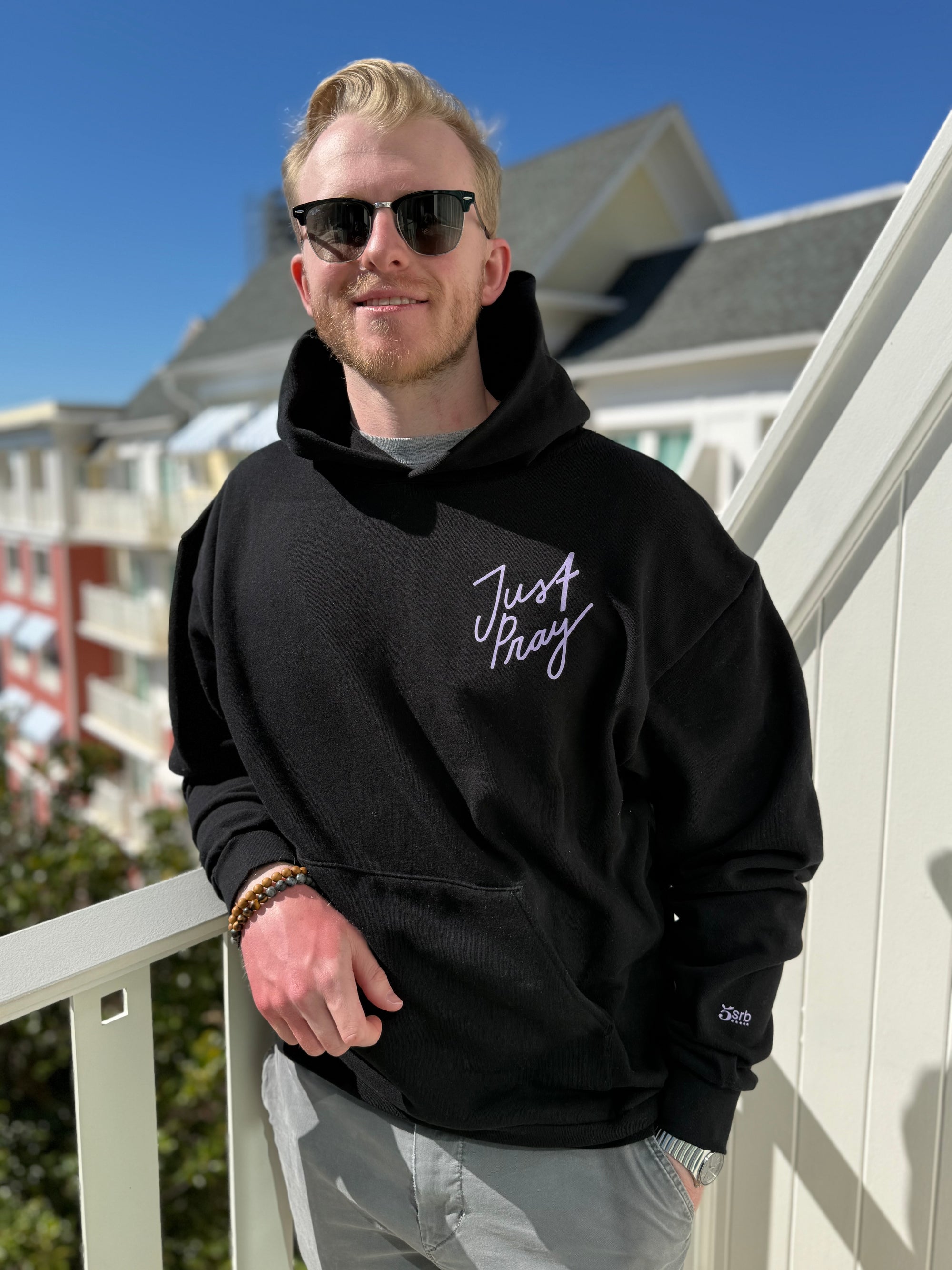 Man wearing a black hoodie with 'Just Pray' text on a balcony