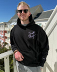 Man wearing a black hoodie with 'Just Pray' text on a balcony