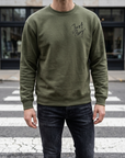 Person wearing a green sweatshirt with text on it, standing on a street.