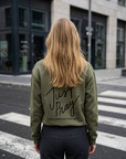 Person wearing a green jacket with 'Just Pray' text on the back, standing on a crosswalk.