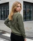 Woman wearing a green sweatshirt with 'Just Pray' text on a city street.