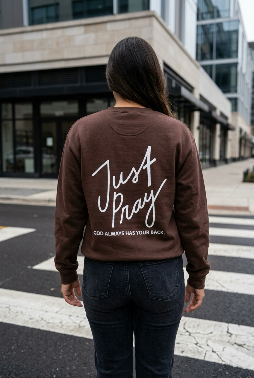 Person wearing a brown sweatshirt with 'Just Pray' text on the back, standing on a city street.
