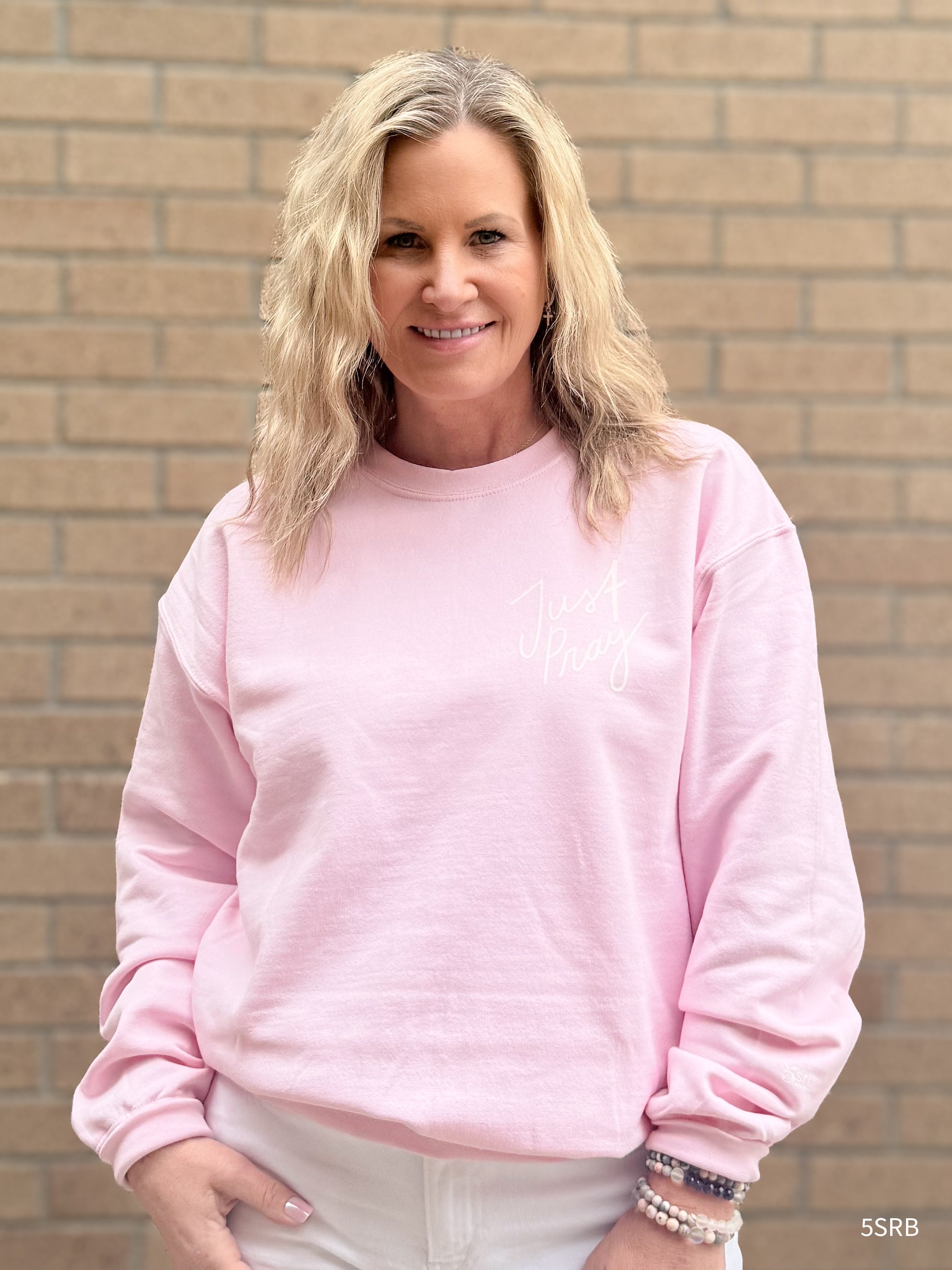 Woman wearing a pink sweatshirt standing in front of a brick wall