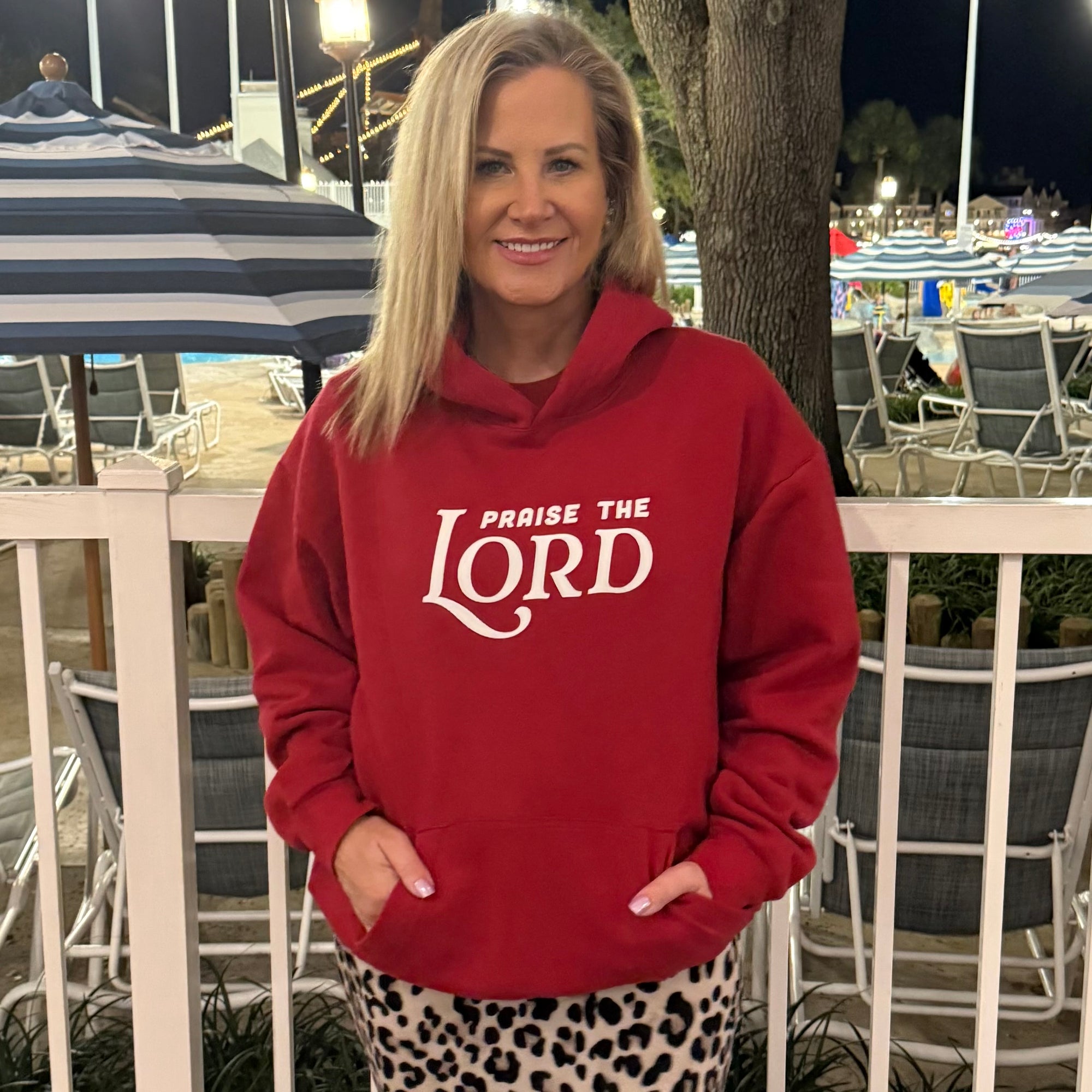 Woman wearing a red hoodie with 'PRAISE THE LORD' text in an outdoor setting.