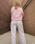 Person wearing a pink sweatshirt with text and light-colored pants against a textured wall.