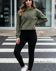 Woman wearing an olive green hoodie with text, black leggings, and white sneakers on a crosswalk.