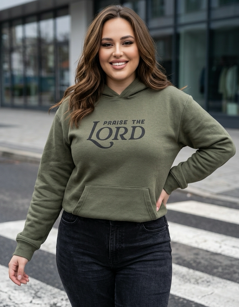 Woman wearing an olive green hoodie with 'Praise the Lord' text on a city street.