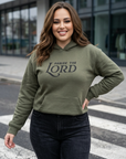 Woman wearing an olive green hoodie with 'Praise the Lord' text on a city street.