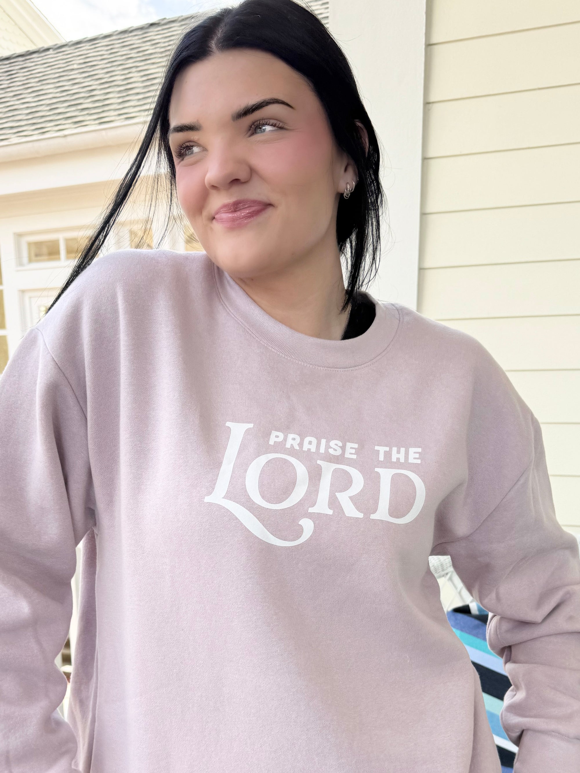 Person wearing a light gray sweatshirt with 'PRAISE THE LORD' text, standing outdoors.