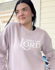 Person wearing a light gray sweatshirt with 'PRAISE THE LORD' text, standing outdoors.