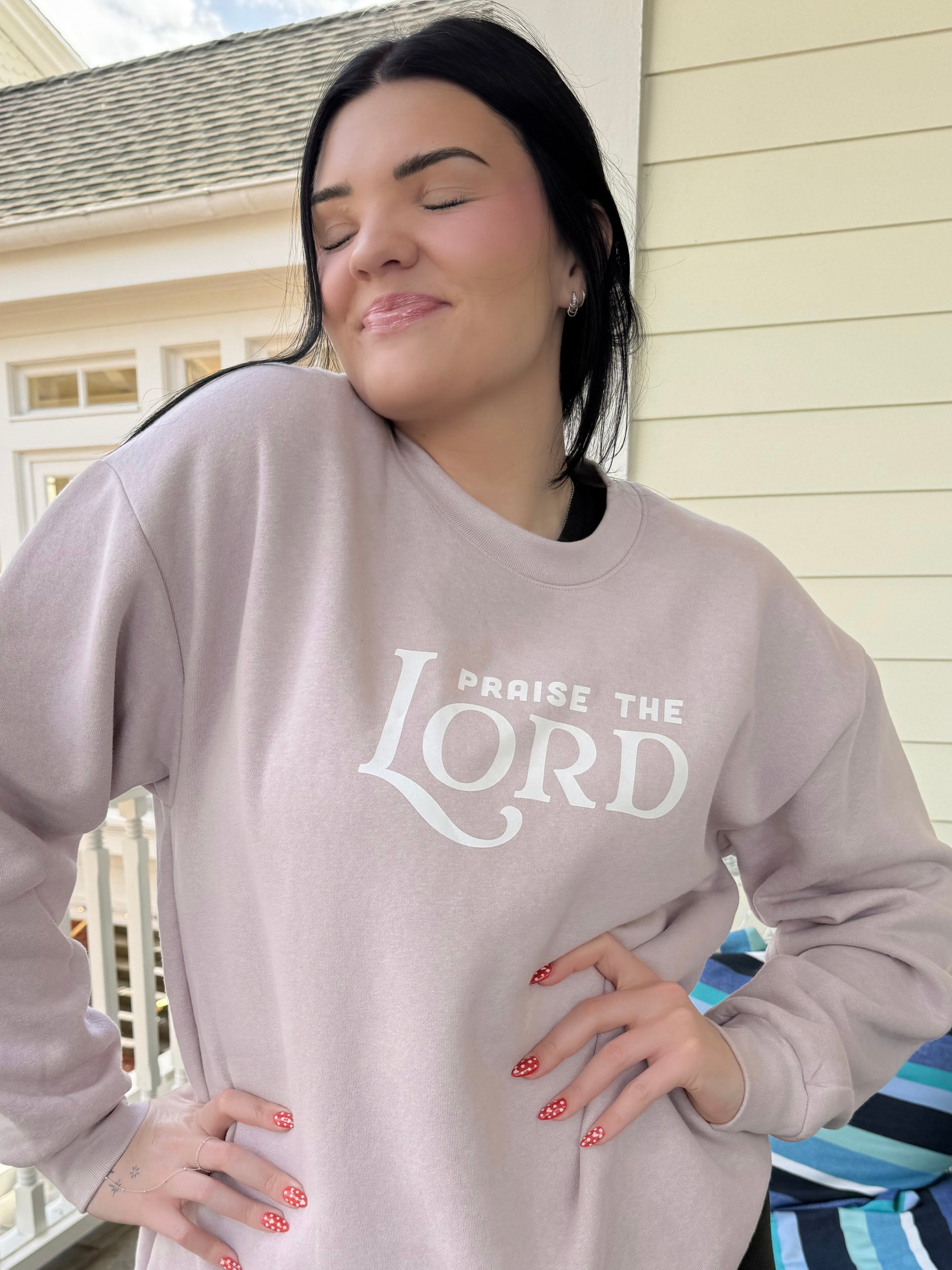 Woman wearing a light gray sweatshirt with 'Praise the Lord' text, standing outdoors.