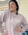 Woman wearing a light gray sweatshirt with 'Praise the Lord' text, standing outdoors.
