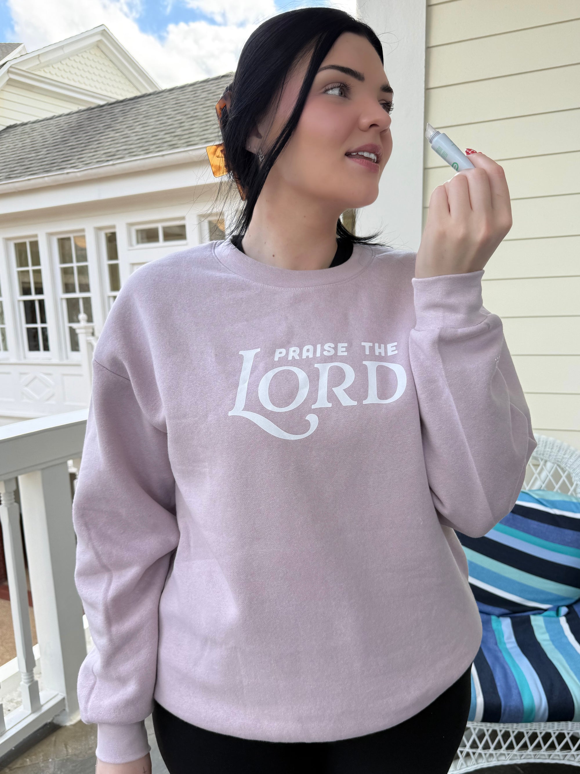 Person wearing a pink sweatshirt with 'Praise the Lord' text on a porch.